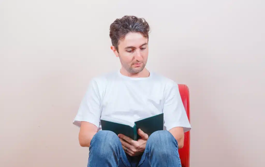 young man t shirt jeans reading book while sitting chair